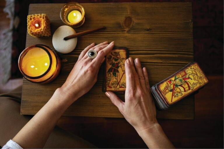 Deux mains posent une carte de tarot sur une table en bois, entre plusieurs bougies allumées